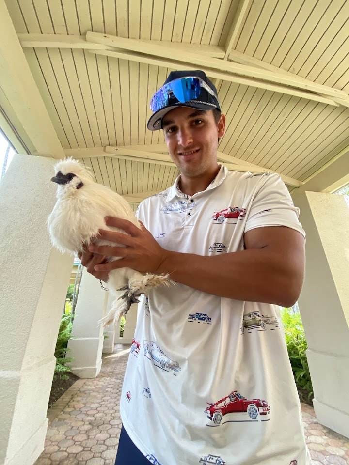 Un jugador de golf sostiene con calma una gallina Silkie blanca de plumaje esponjoso, durante un torneo de golf en Puerto Rico