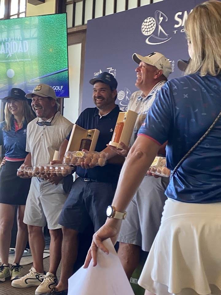 Ganadores del torneo SME Golf sonriendo mientras sostienen docenas de huevos de punto.pio como premio